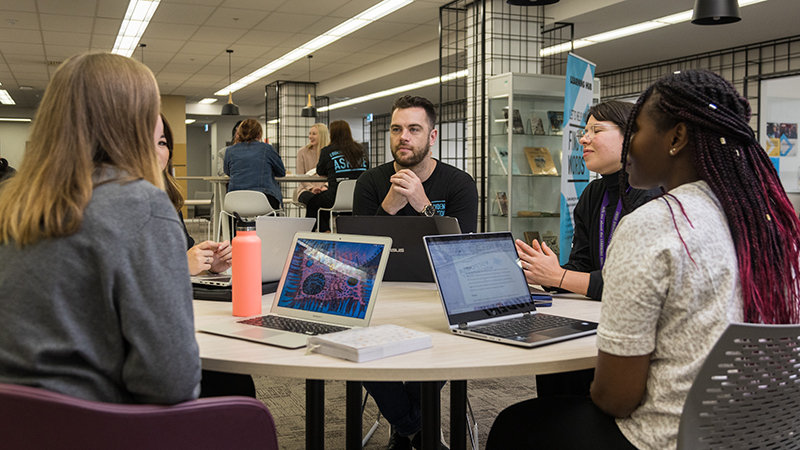 Study group, multicultural, with laptops, in lively discussion in the VU library