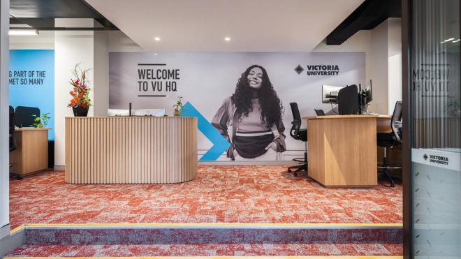  A carpetted room with reception desks and seating areas. A large Victoria University banner is in the background, welcoming students to the campus.