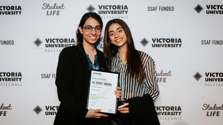  two smiling students holding a leadership award