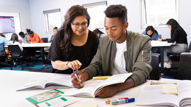 A student learning in a classroom, getting assistance from a teacher.