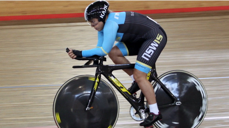 Female athlete cycles on indoor track, in professional cycling gear