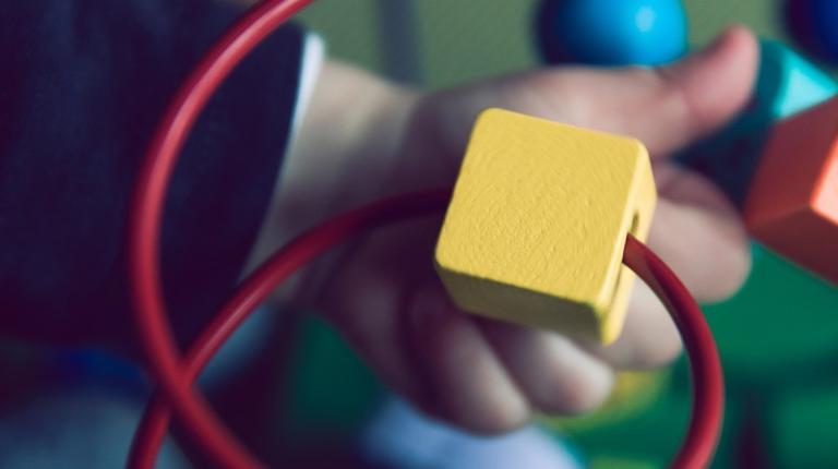 Toddler hand playing with bright wooden toy