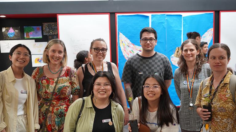 Group of women and men smiling at the camera, with student art in the background