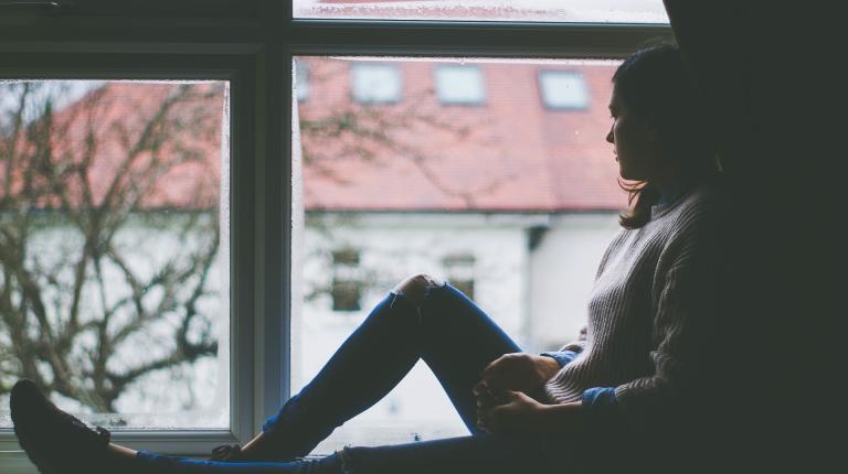Young woman sitting on a windowsill staring out 