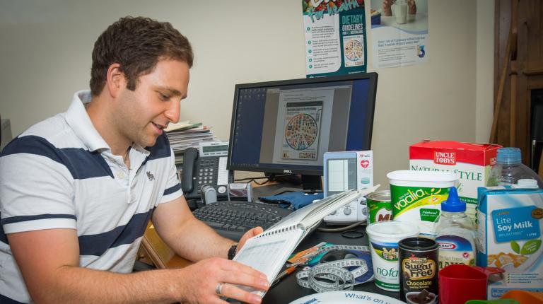 Master of Nutrition student at a computer desk with different foods and charts