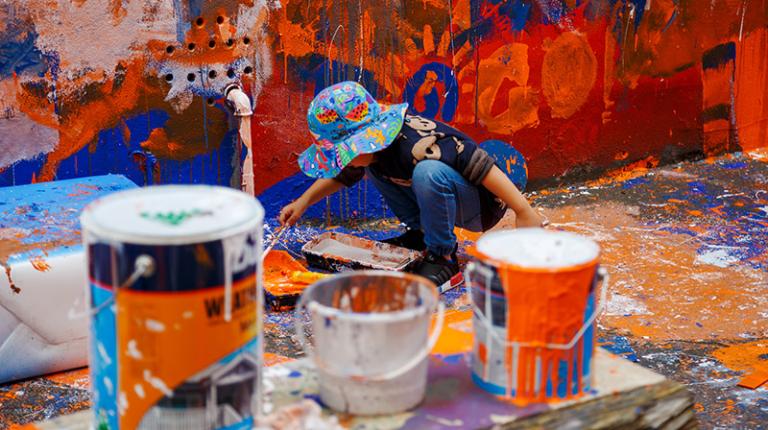 toddler painting an outdoor wall in bright colours