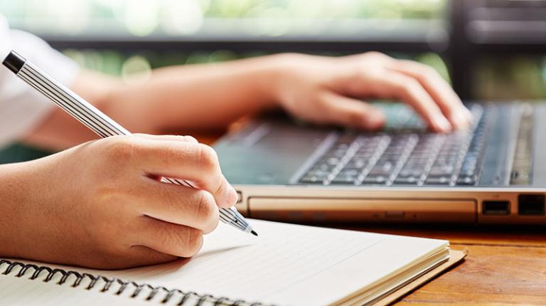  A student writes notes off a laptop while studying.