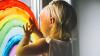 Child fingerpainting a rainbow onto a window.
