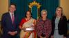 Group of people stand in front of colourful curtain, including woman in traditional Indian dress, holding award