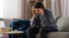  woman depressed on couch, holding head with pill bottle in front of her