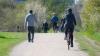  People in winter clothes walking and riding a bike in a park.