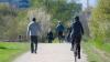  People in winter clothes walking and riding a bike in a park.