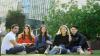 Five diverse, smiling students sitting on the grass at Footscray Park Campus