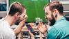  Two friends excitedly checking their sports betting app on their phone, as they watch a soccer match together