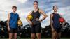   Three women stand posed on a football field, each holding a football.